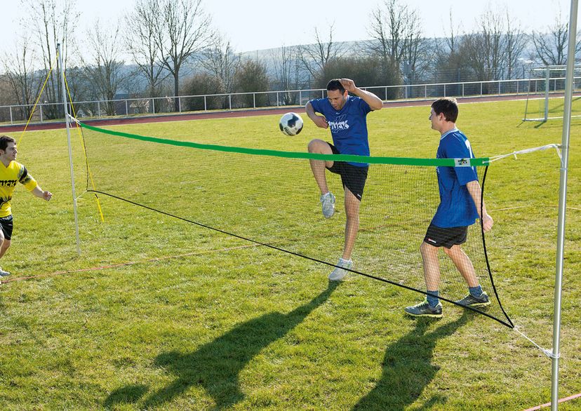 Fußballtennisnetz mir 3 Spielern auf der Wiese