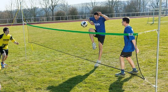 Fußballtennisnetz mir 3 Spielern auf der Wiese